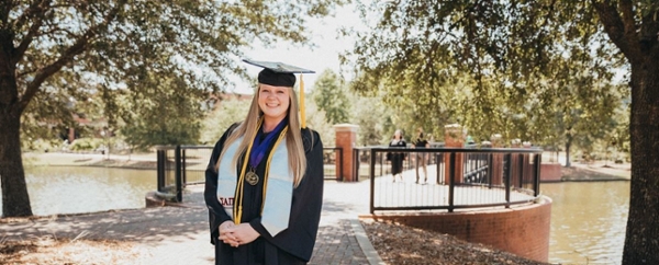 Rebecca Symone Caldwell, President’s Scholar for the Class of 2022, standing by the bridge on the Macon Campus in her cap and gown for graduation.